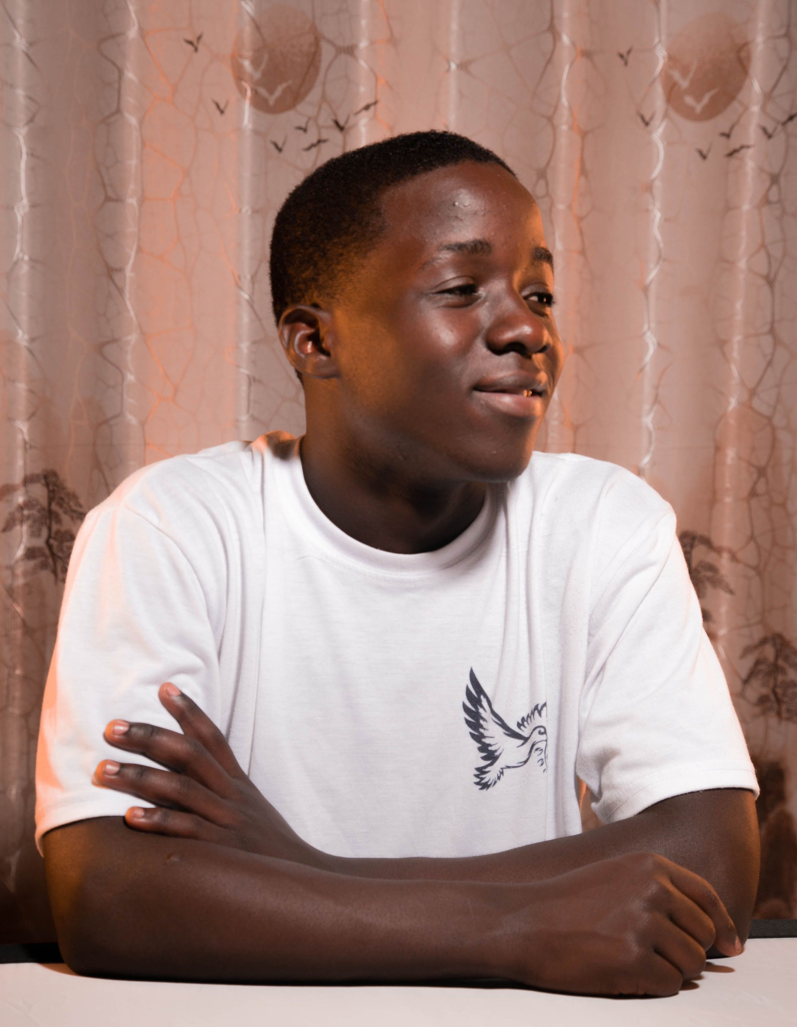 Young male in a white t-shirt with a bird design, deep in thought against a patterned background.