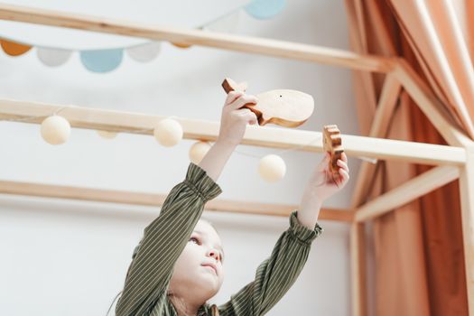 Young child in a playroom reaching up with wooden toys in hand.