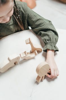 一个孩子穿着绿色连衣裙，在室内的白色桌子上玩木制动物玩具