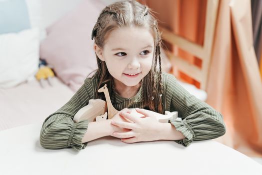 A joyful little girl with braids holds a wooden toy in a cozy indoor setting.
