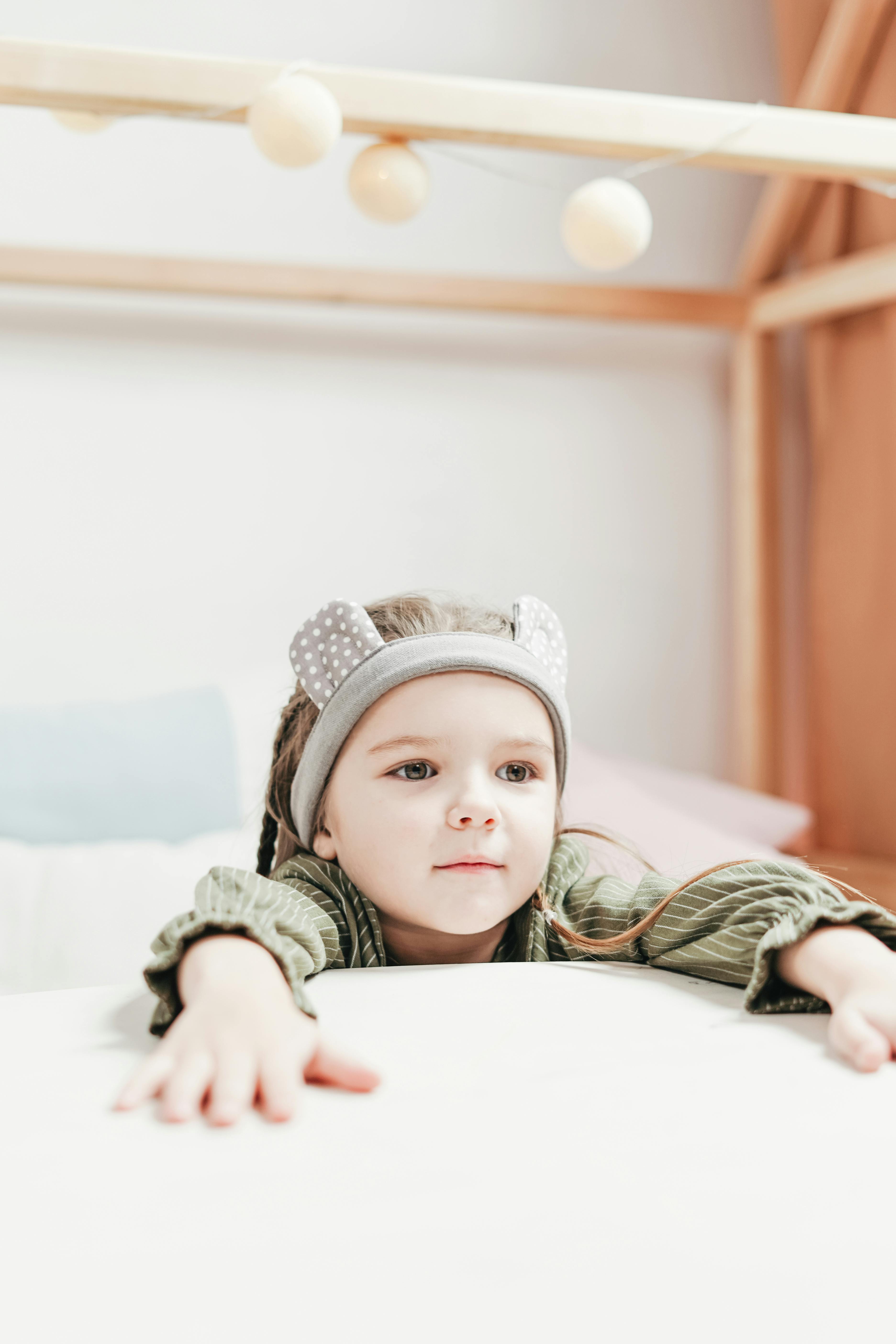 child in green and white jacket lying on bed