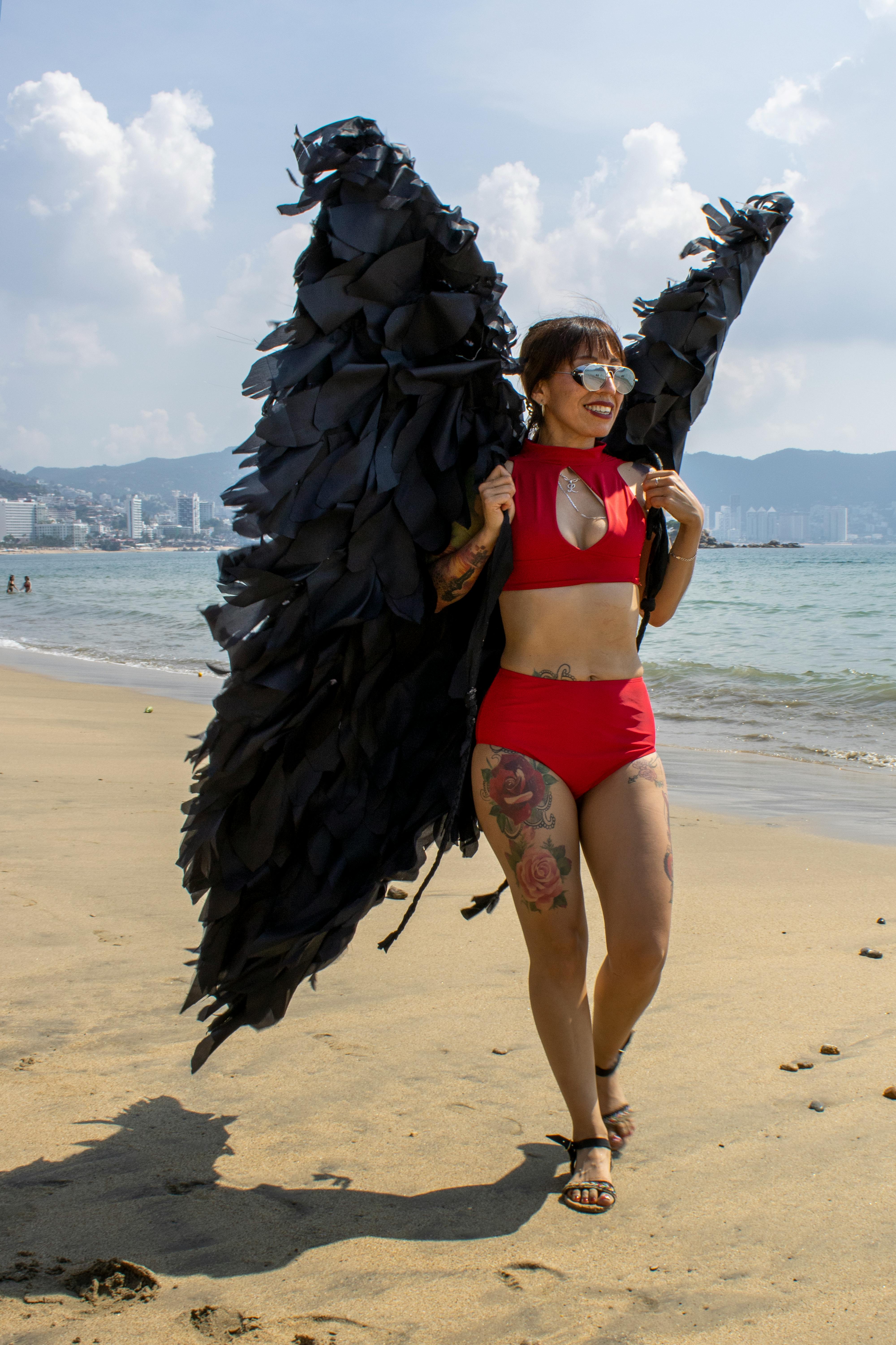 무료 멕시코 아카풀코 해변에서 빨간색 비키니에 검은색 깃털 장식 의상을 입고 미소 짓는 여성. 스톡 사진