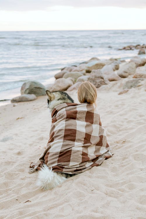 Woman in White and Brown Scarf Sitting on Beach with Dog