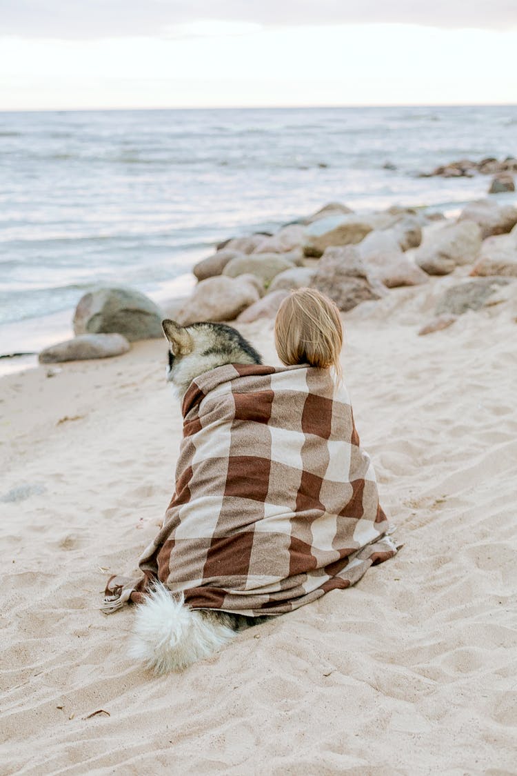 Woman In White And Brown Scarf Sitting On Beach With Dog