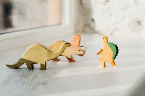 Free A delightful set of wooden dinosaur toys basking in natural light by the window, capturing playful innocence. Stock Photo