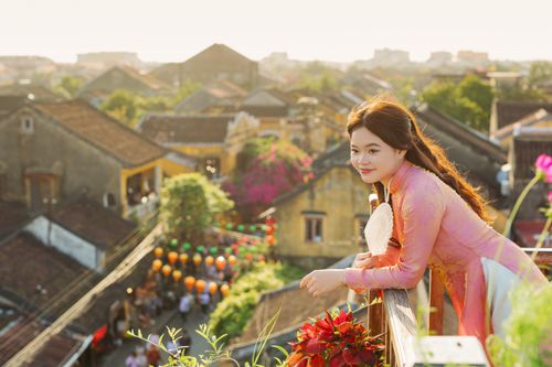 Free Woman in traditional Vietnamese dress enjoying the view over Hội An from a balcony. Stock Photo