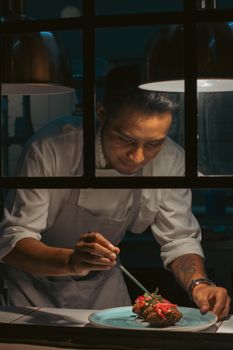 A focused chef meticulously plates a gourmet dish under warm lighting in a professional restaurant kitchen.