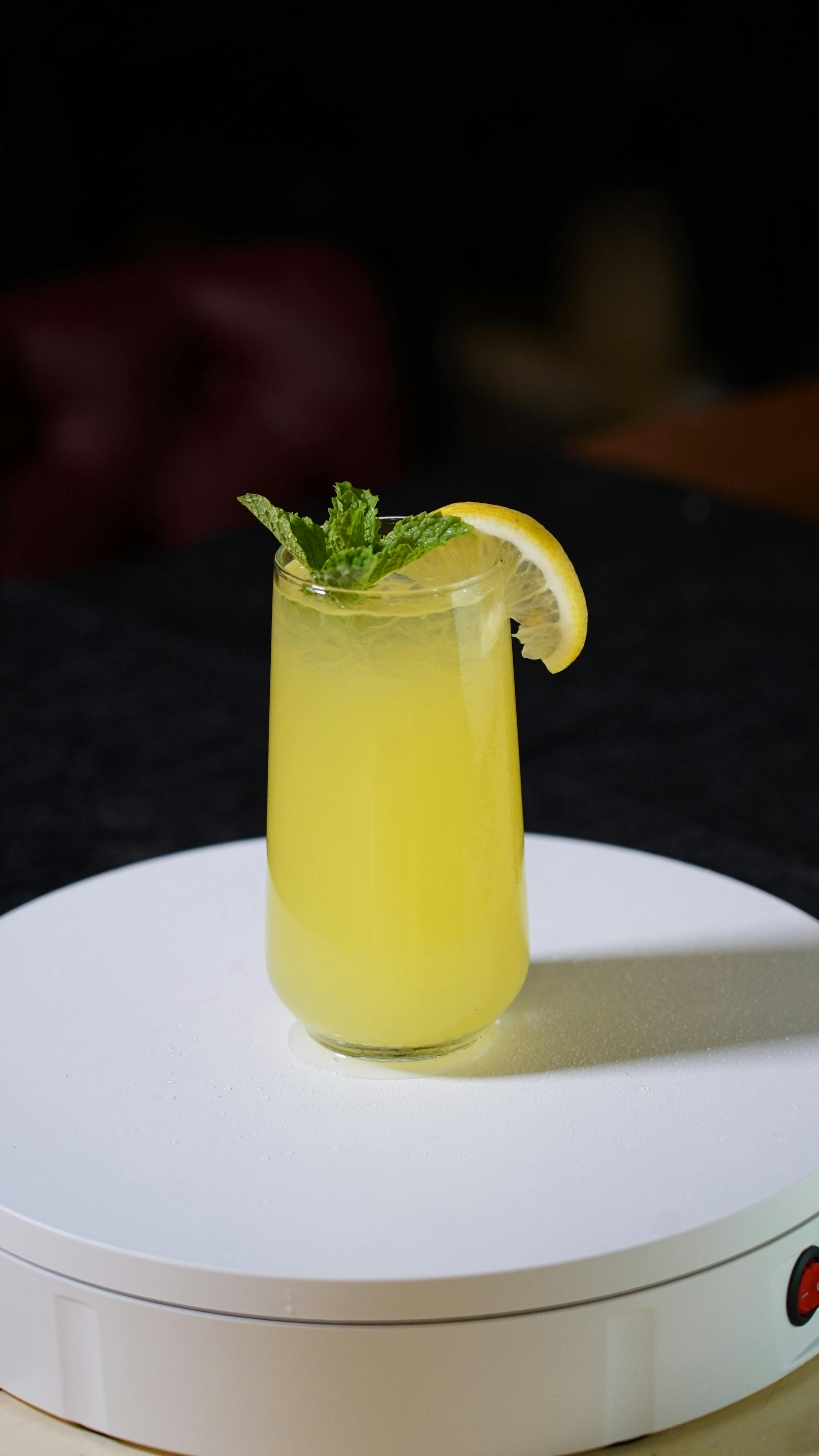 무료 레몬과 민트로 장식된 레몬 민트 음료가 담긴 큰 유리잔이 흰색 테이블 위에 놓여 있습니다. 스톡 사진