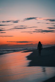 A solitary figure walks along the beach at sunset, surrounded by vibrant, warm colors.