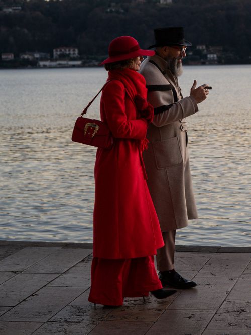 Free Stylish couple in red and beige coats walking by a serene lakeside during twilight. Stock Photo