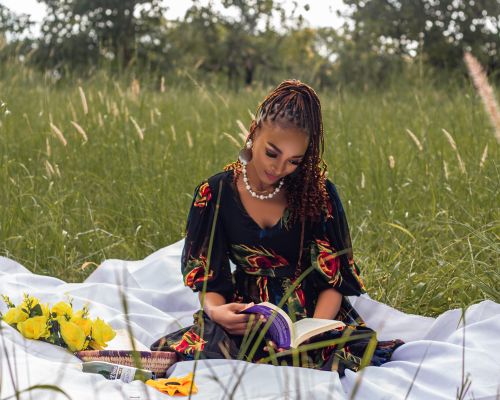 Free Woman enjoys a sunny day outdoors, reading a book in a serene meadow with yellow flowers nearby. Stock Photo
