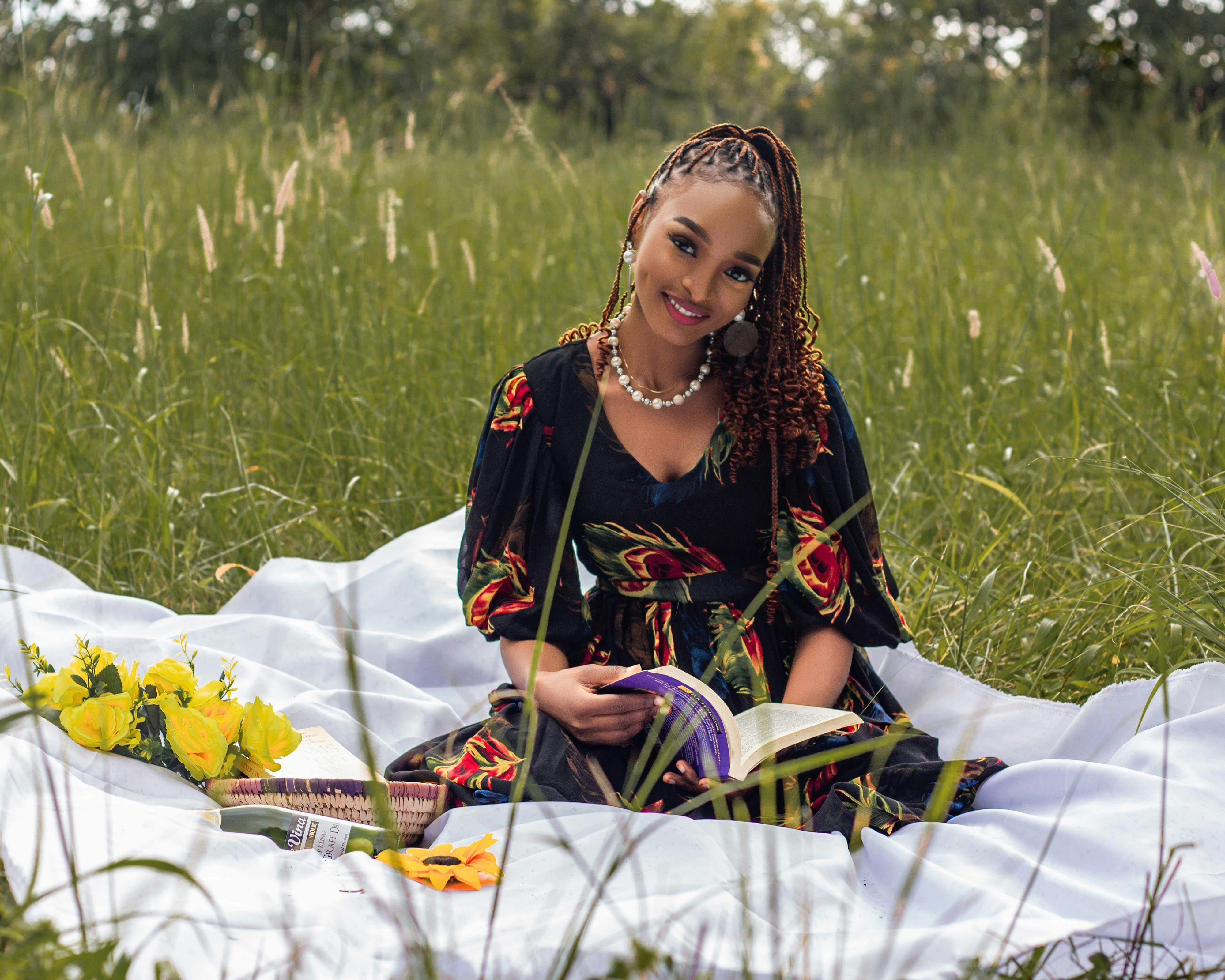 Безкоштовне Жінка насолоджується спокійним післяобіднім читанням на ковдрі серед пишної сонячної луки. стокове фото