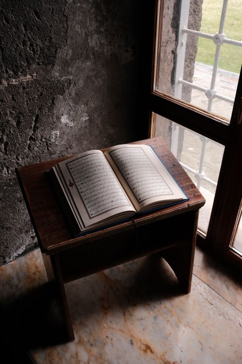 Free A book rests on a wooden stand by a window in a rustic setting, evoking a calm and reflective mood. Stock Photo