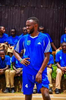 A male athlete in a blue soccer uniform on a sunny sports field with spectators in the background.