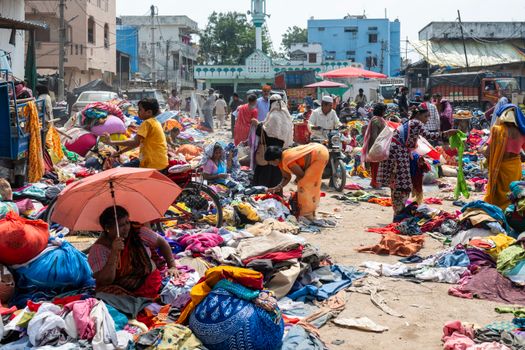 Vibrant market scene where people shop for clothes amidst colorful fabric piles.