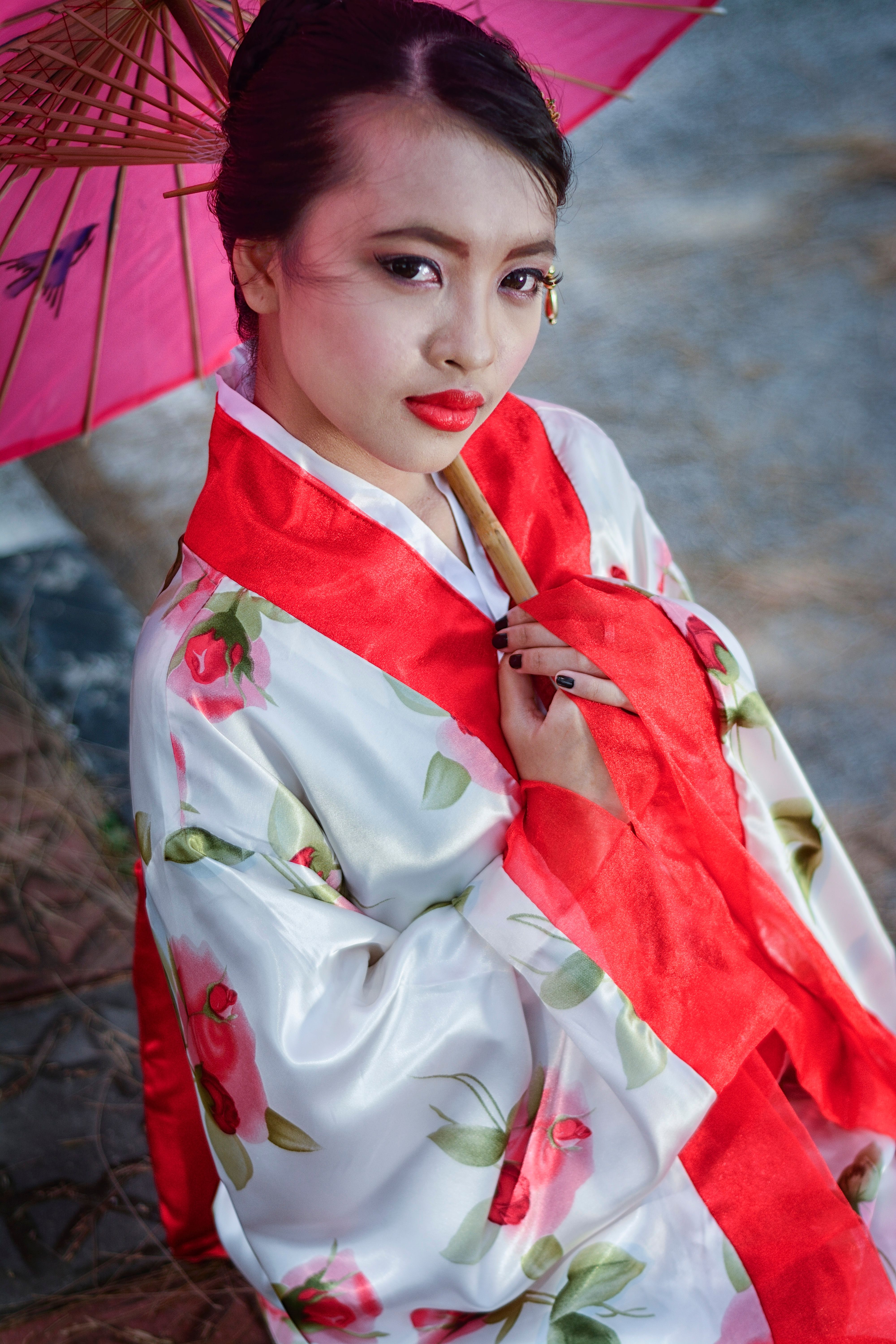 Elegant portrait of a woman in a floral kimono holding a pink parasol outdoors.