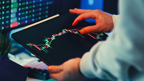 A close-up of a person using a tablet to analyze stock market trends and charts indoors.