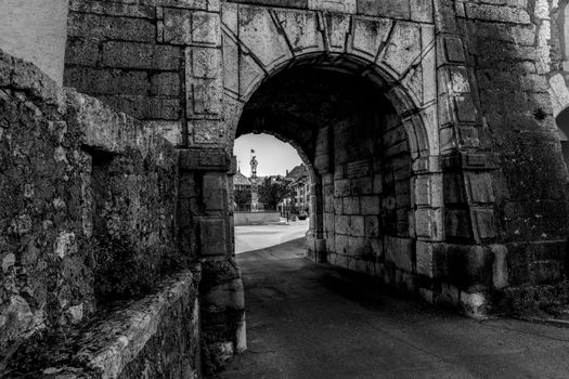 Black and white photo of a historic stone archway leading to a Swiss town square.