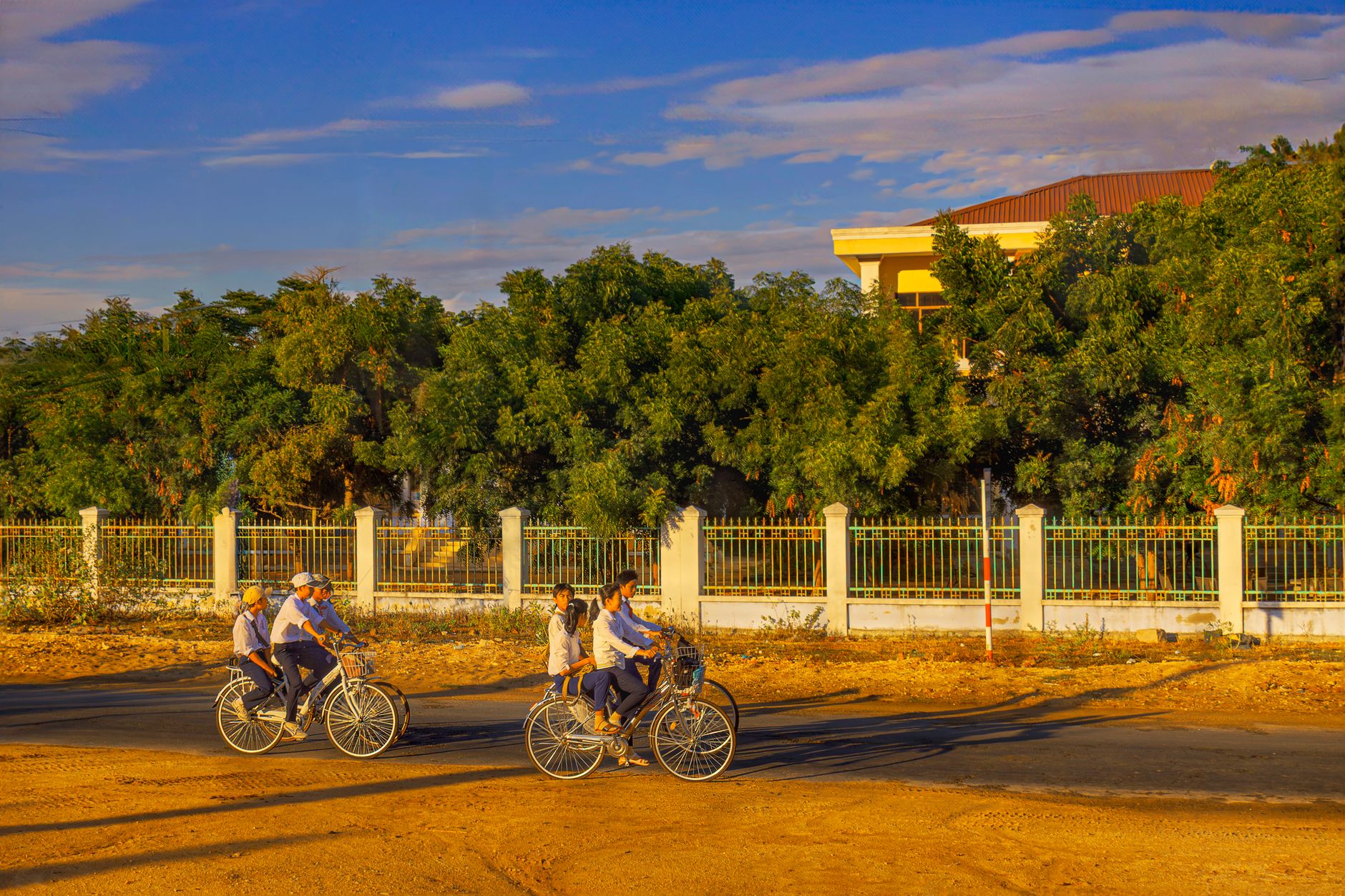 Children biking under a vivid sky in Vietnam, enjoying a sunny day outdoors.