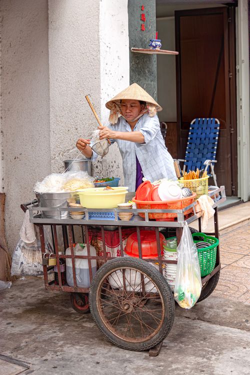 Free A Vietnamese street vendor preparing food on a traditional cart in an urban setting. Stock Photo