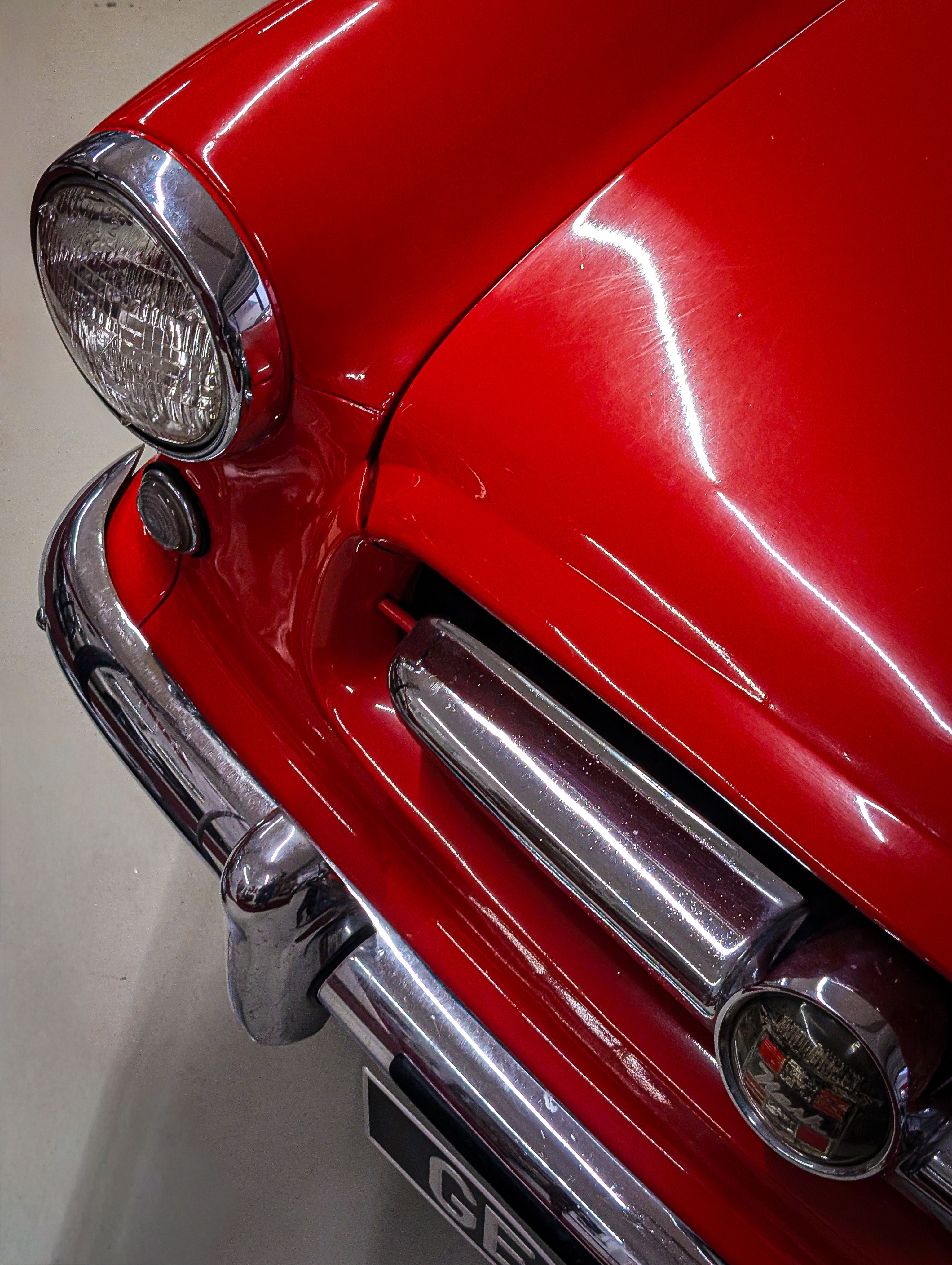 Detailed shot of a vintage red car's headlight and grill, showcasing classic automotive design.