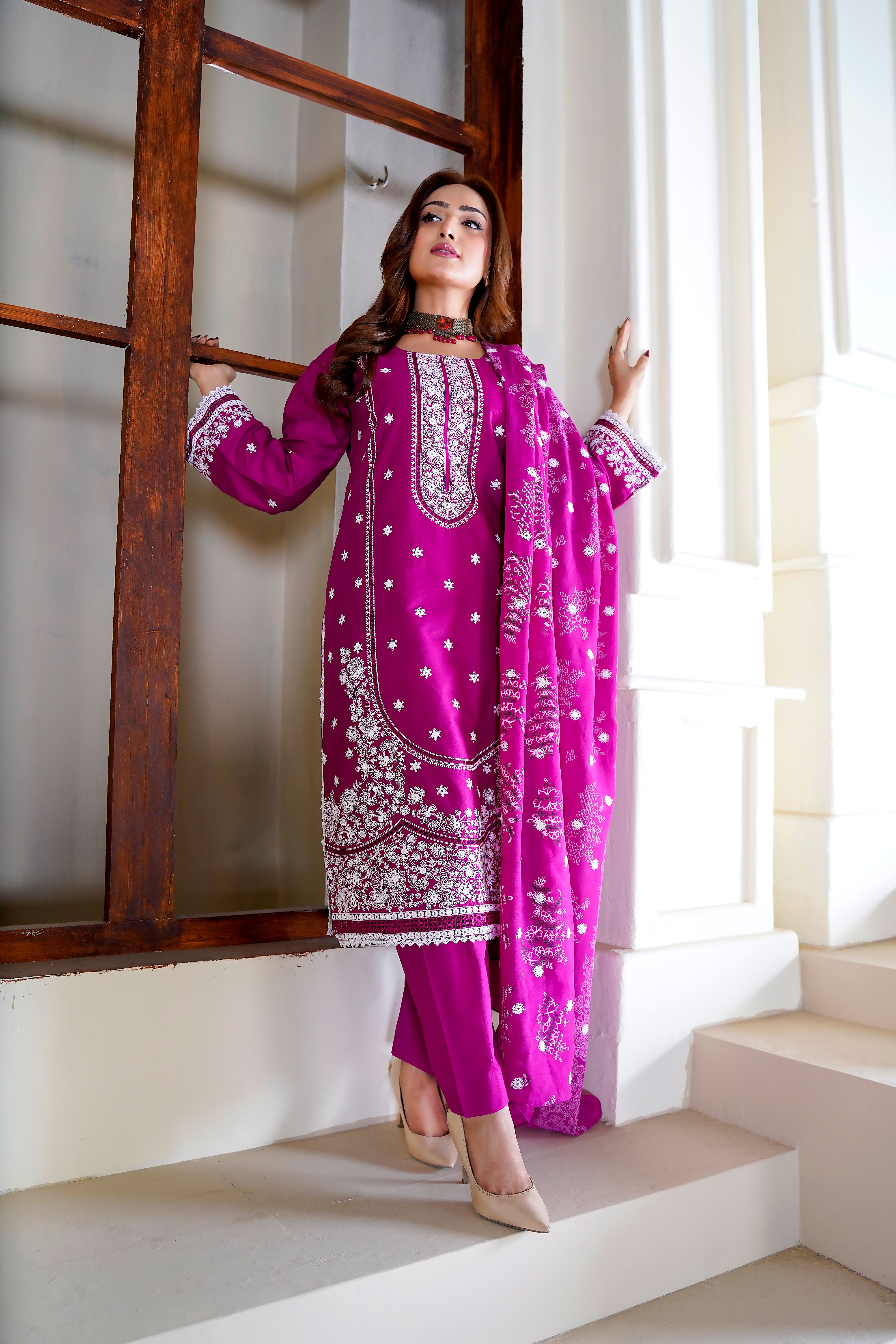 Model showcasing an elegant embroidered pink dress in a Lahore architectural setting.