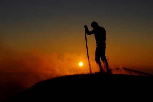 Free A dramatic silhouette of a hiker with a staff at sunrise on a mist-covered mountain peak. Stock Photo