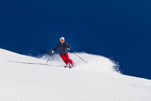 Free An adult skier in red pants skiing downhill on a snowy slope under a clear blue sky. Stock Photo