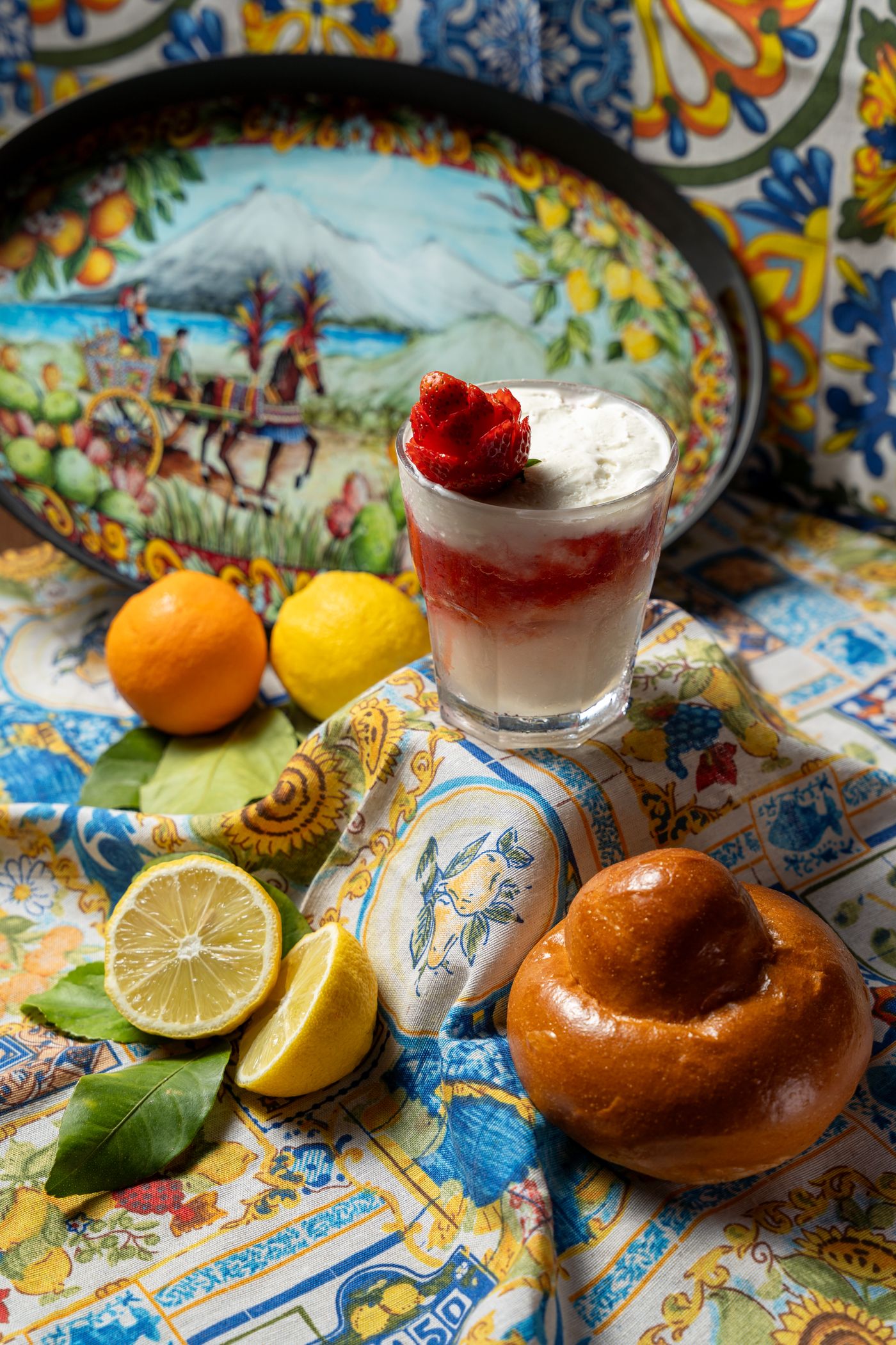 A tall glass of granita topped with fruit, on a painted ceramic table