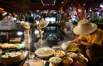 Thai street vendor preparing noodles at a vibrant indoor market stall.