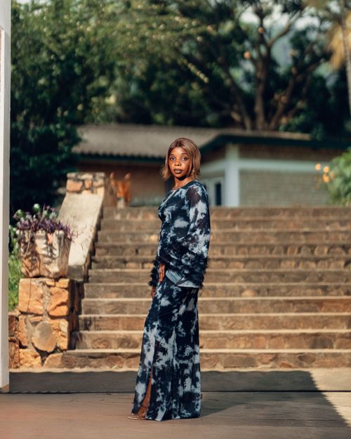 Free Stylish woman poses in long tie-dye dress on stone steps in a sunny outdoor setting. Stock Photo