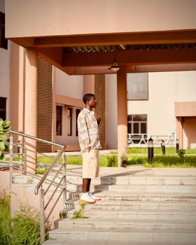 Young man in casual attire standing outdoors near a modern building in Kano, Nigeria.