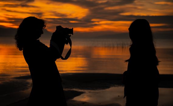 Silhouetted photographer captures a scenic sunset by a tranquil sea shore.