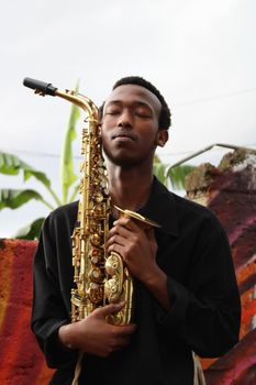 Portrait of a young man with a saxophone against a vibrant wall in Kigali, Rwanda.