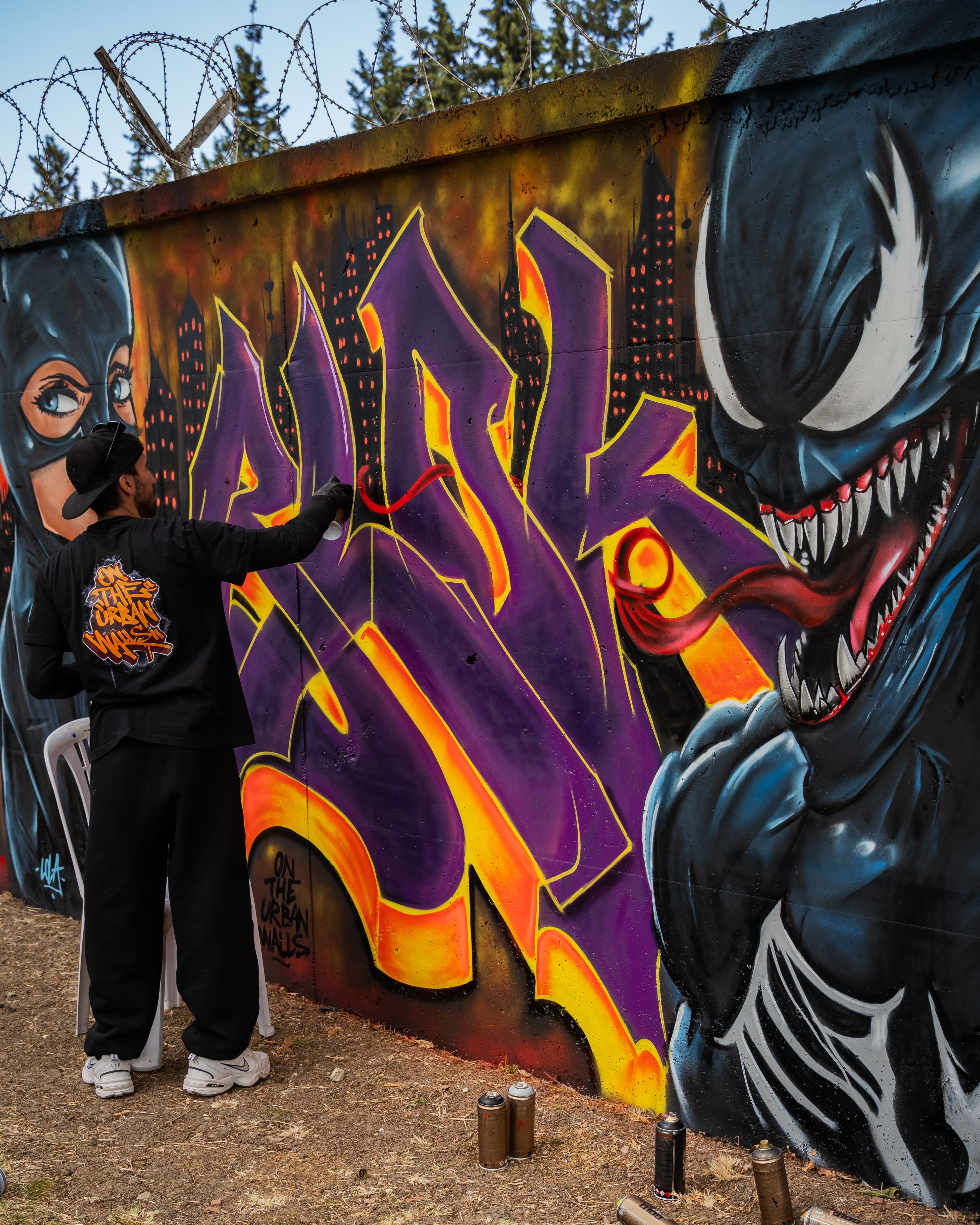 Street artist creating vibrant graffiti art on a wall outdoors, featuring comic book characters.