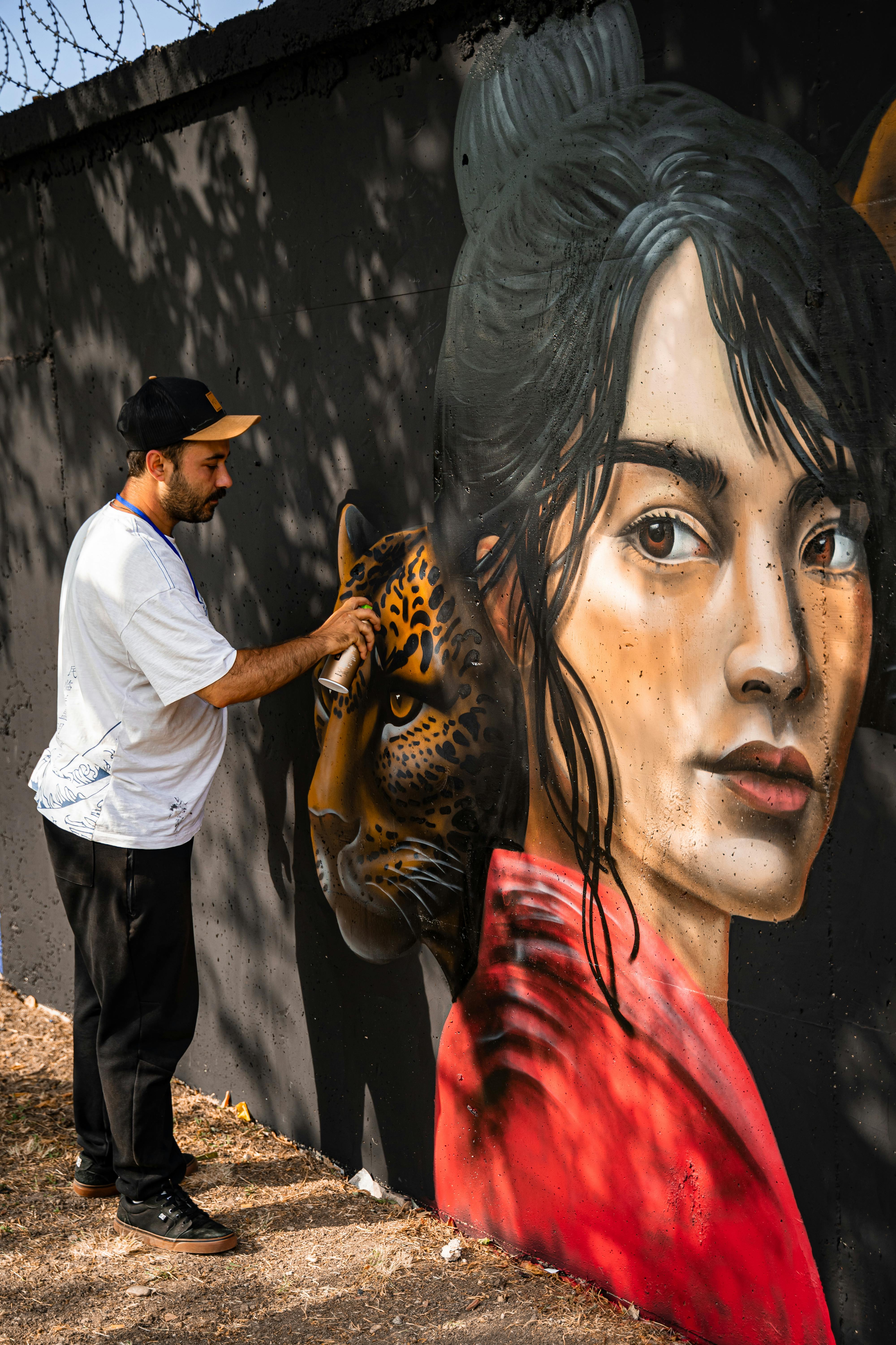 Street artist creating a colorful mural depicting a woman and jaguar on a city wall.