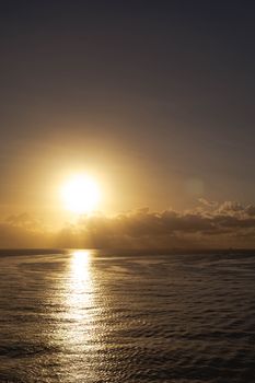 Dramatic golden sunset over the ocean with clouds and gentle waves reflecting the sun.