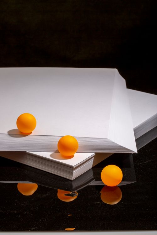 Free Vivid orange balls arranged on white paper against a dark background, featuring reflections. Stock Photo