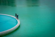 Two people fishing on a platform at La Serena, Chile, surrounded by turquoise water under a clear sky.