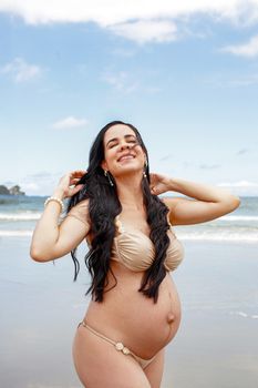 Pregnant woman smiling joyfully in a bikini on a sunny beach day, embracing motherhood.