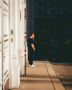 Casual street scene in Vienna with a man standing against a sunlit facade. Contrast of light and shadow.