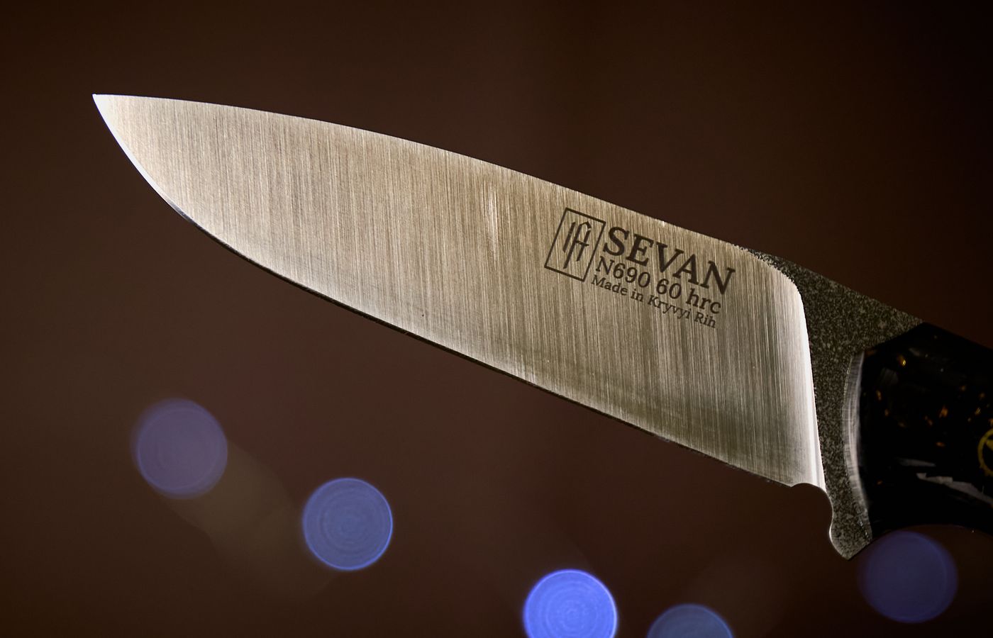 Detailed close-up of a Sevan knife blade featuring bokeh background for a dramatic effect.