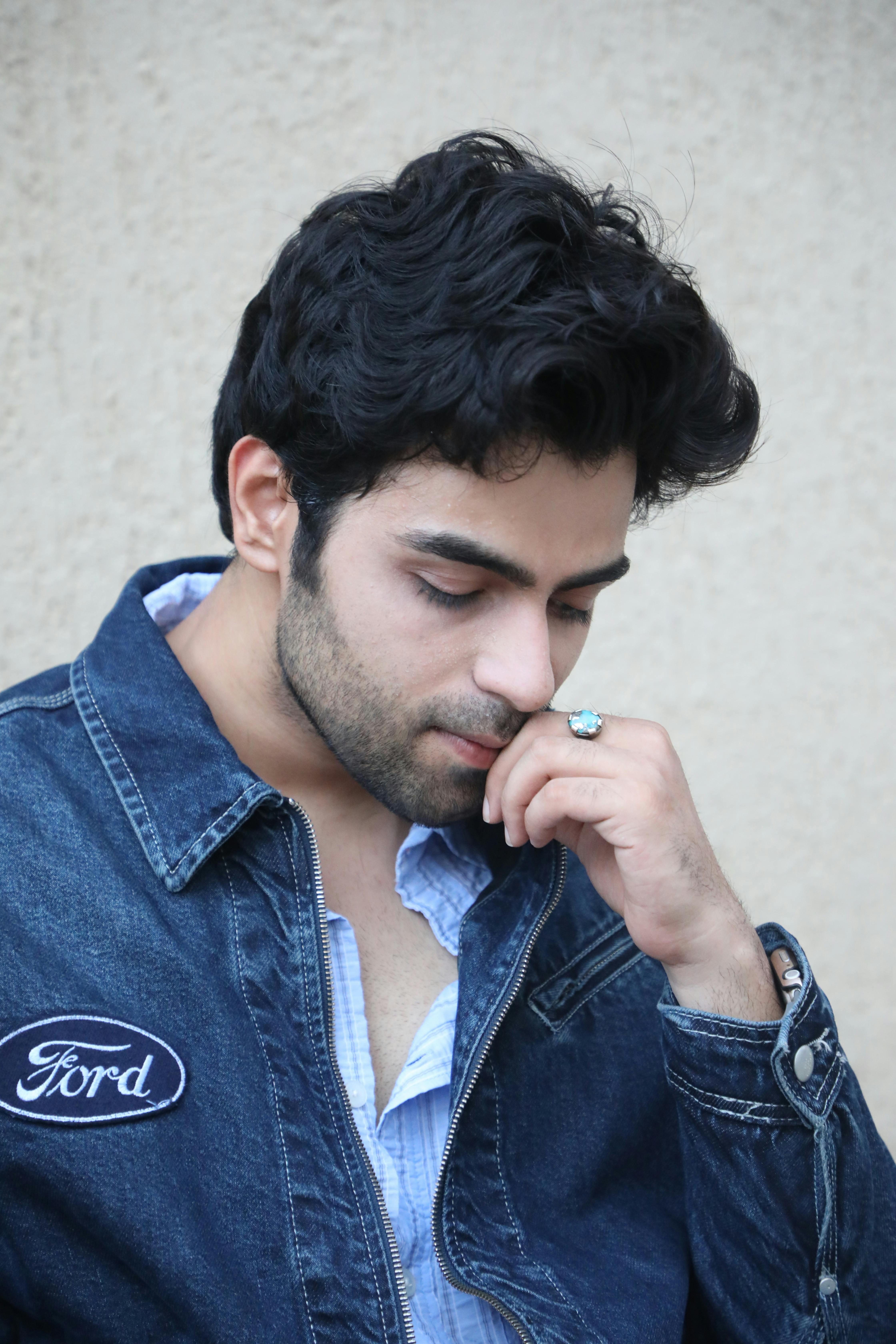 Thoughtful young man in a denim jacket with Ford patch, posing against a beige background.
