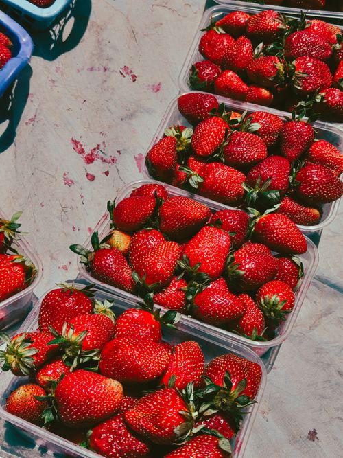 Free Vibrant red strawberries displayed in plastic containers at a sunny outdoor market. Stock Photo
