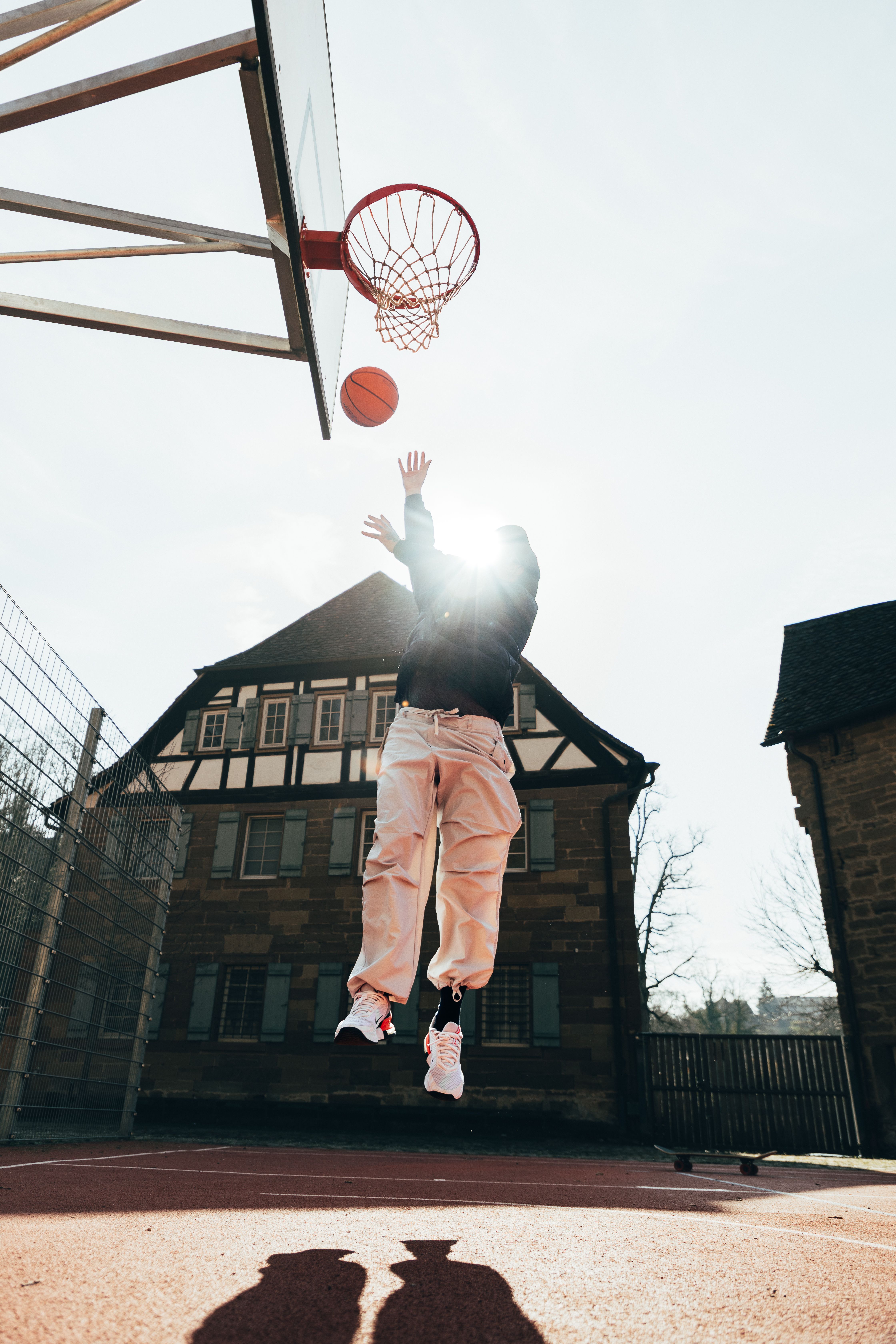 Action shot of a person jumping to make a basketball hoop outdoors.