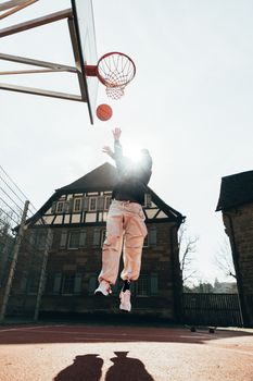Action shot of a person jumping to make a basketball hoop outdoors.