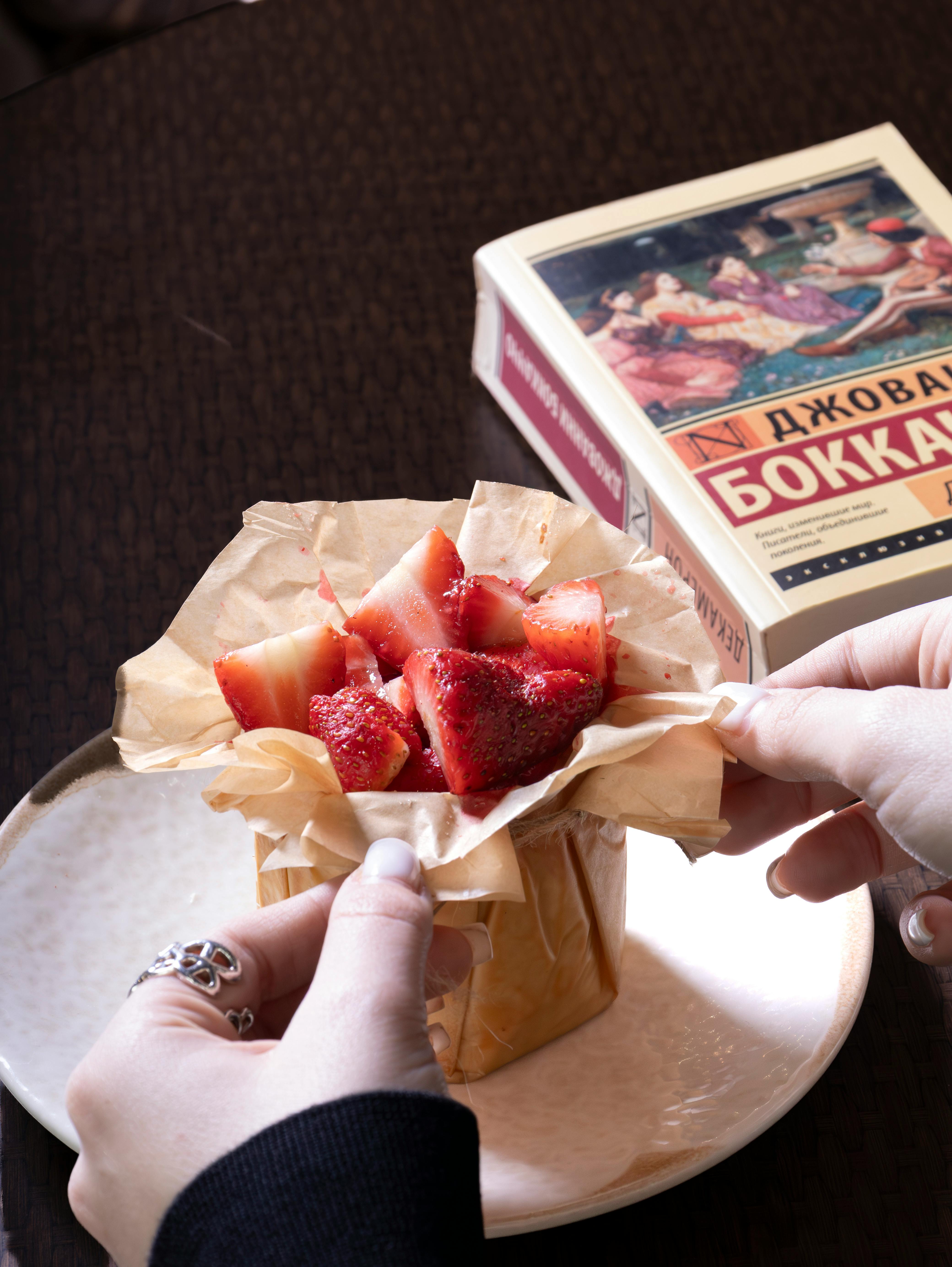Hands Wrapping Strawberries in Vintage Book Setting