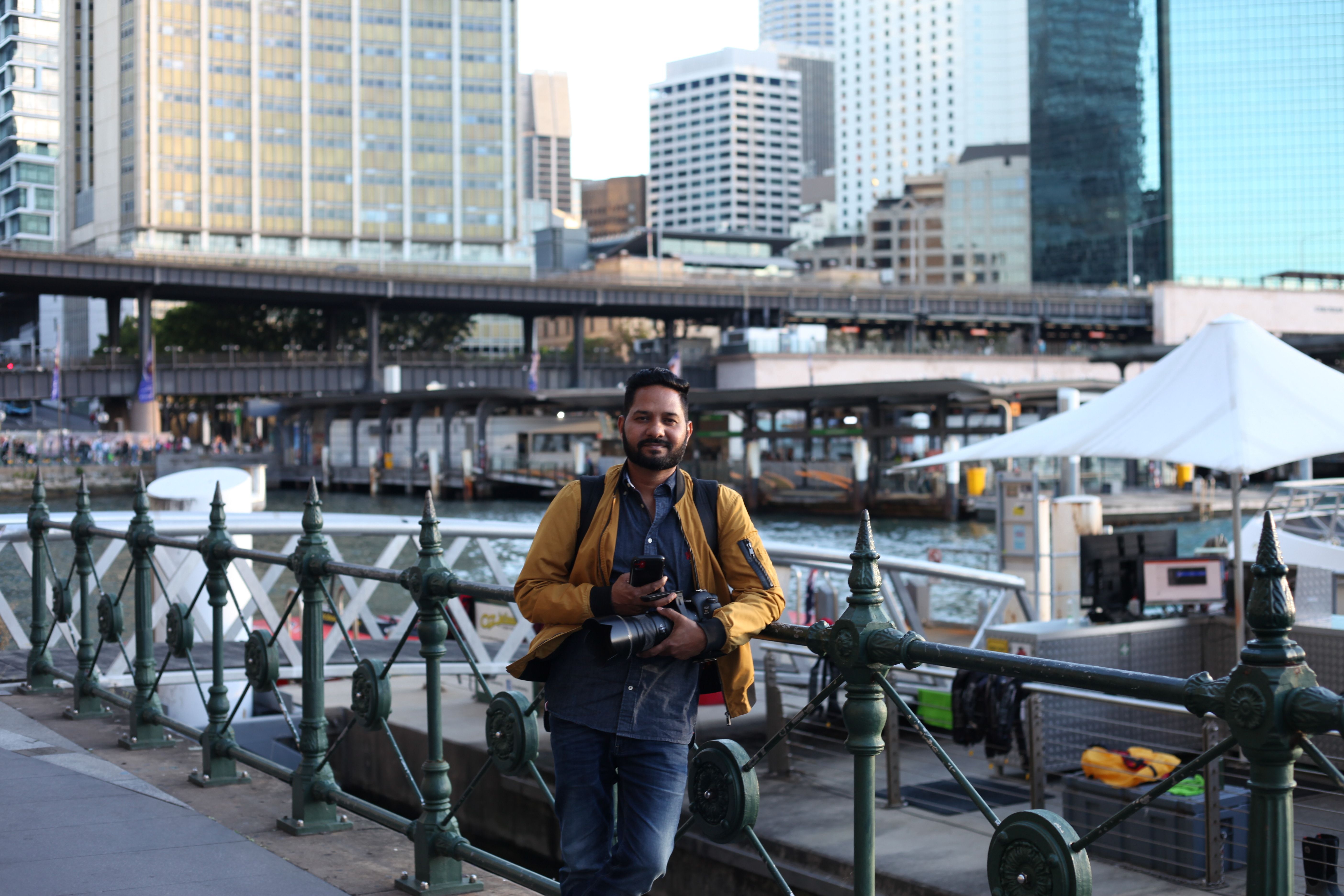 Photographer holding camera by urban waterfront with city skyline in background