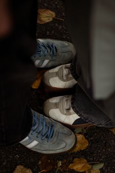 Two pairs of casual sneakers on a leaf-strewn pavement during autumn.