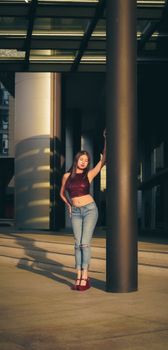 Fashionable young woman in casual attire poses confidently near modern architectural column in daylight.